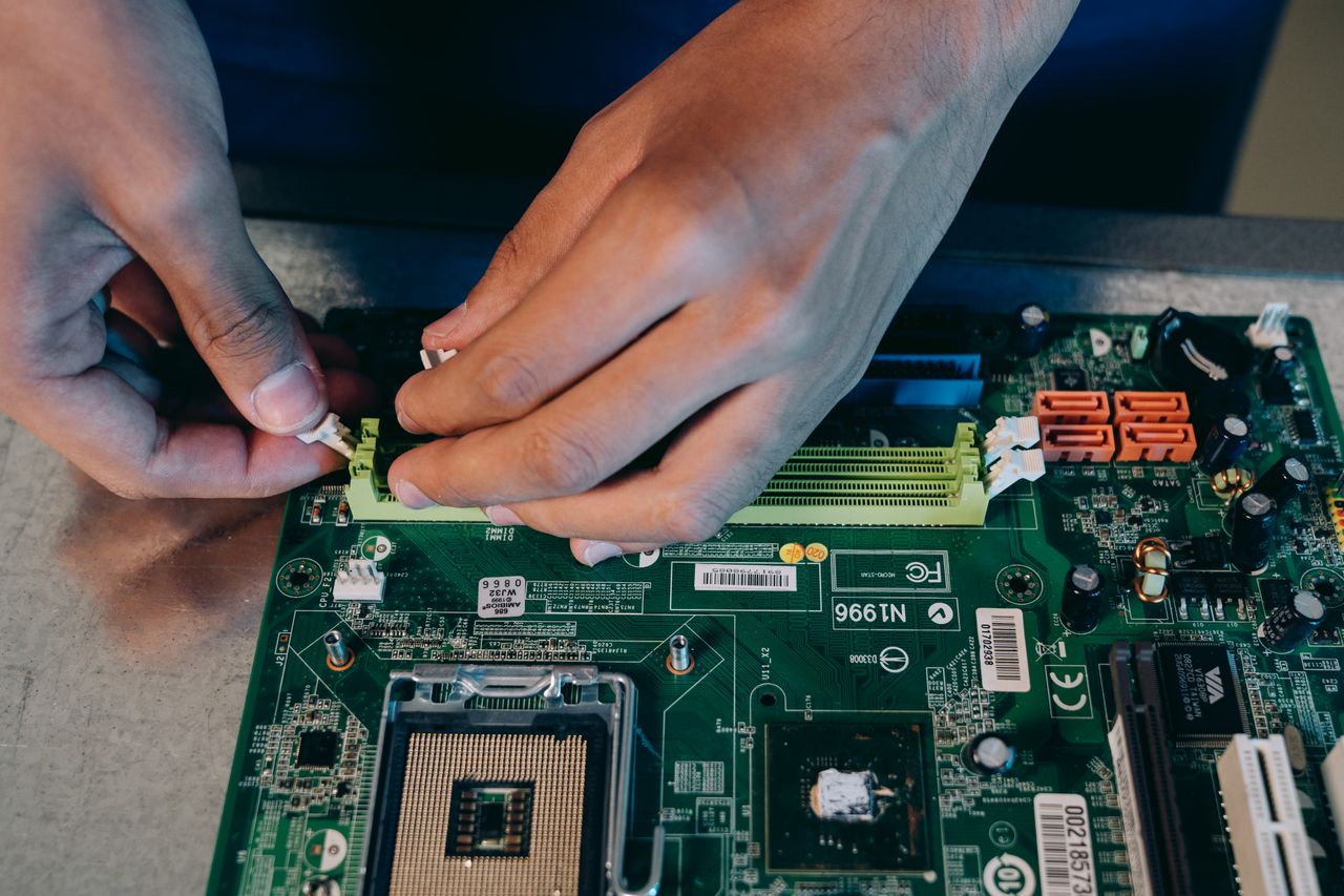 Hands carefully assembling a computer motherboard, showcasing technical craftsmanship in electronics.